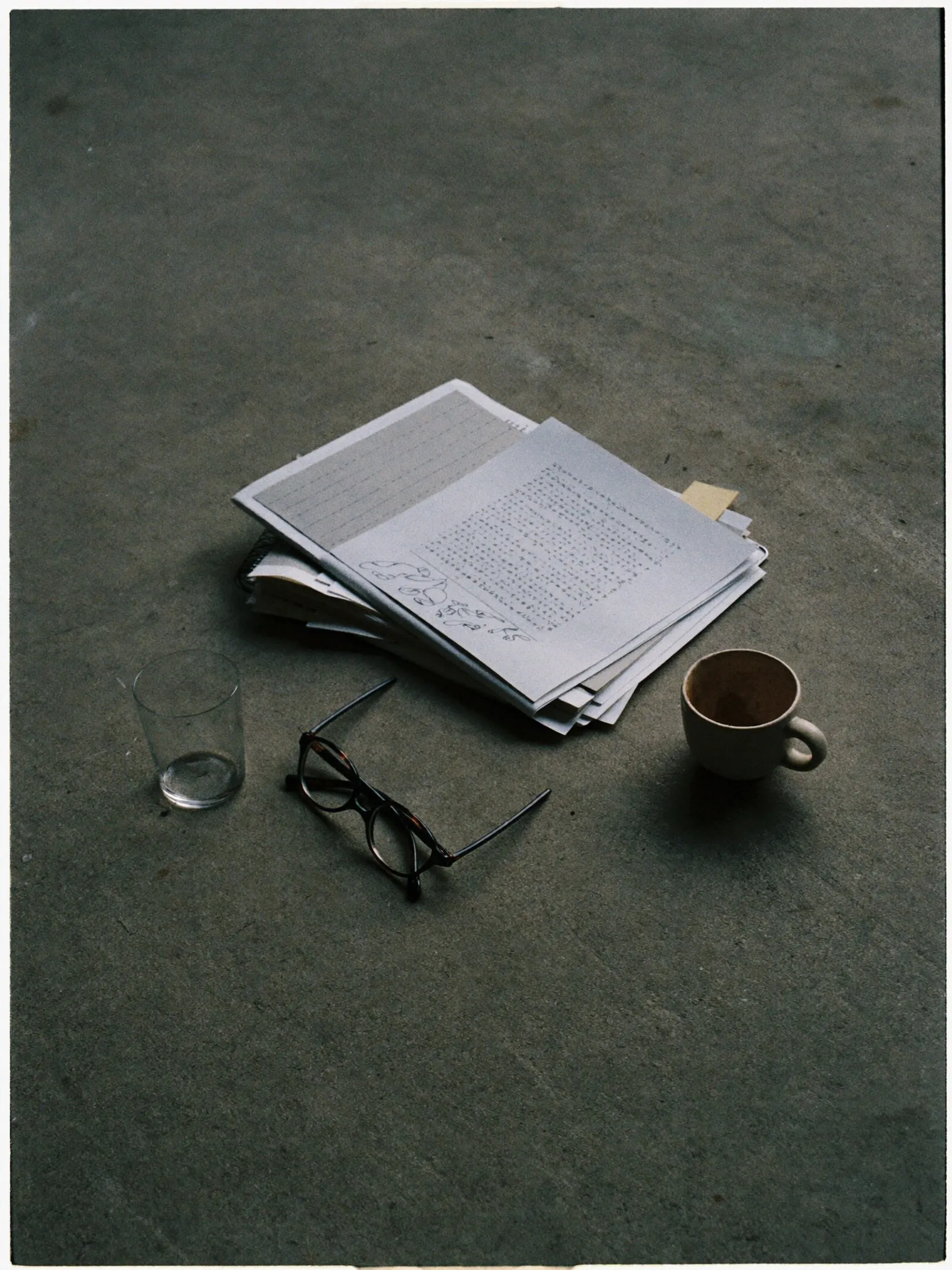 Papierstapel, Brille und Tasse auf einer Betonfläche